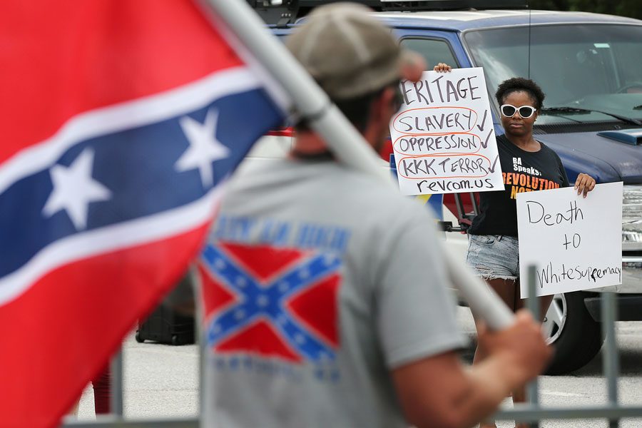 A woman stands with a sign protesting a man flying a Confederate flag in Georgia.